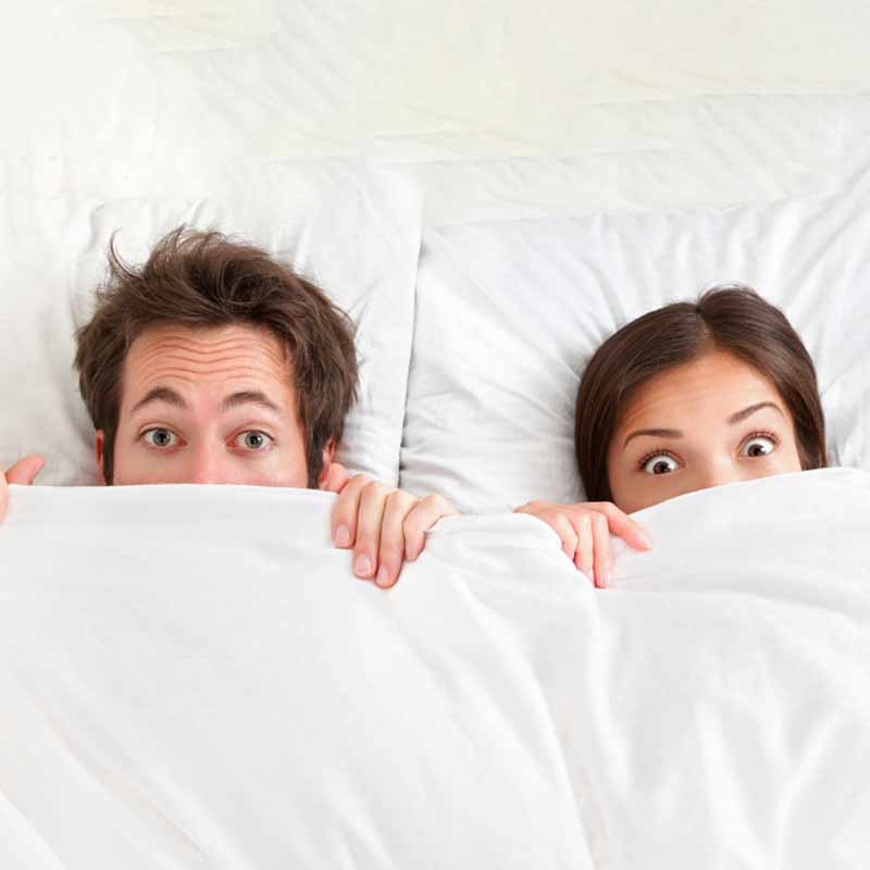 a man and a woman underneath the blankets peeking at the camera