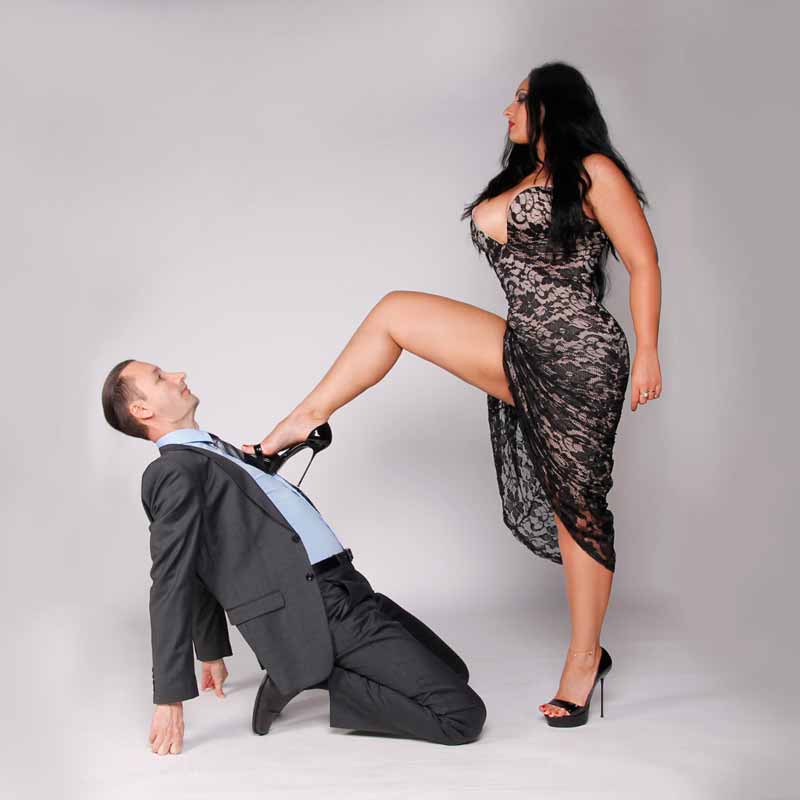 a curvy mistress dominating a man on his knees in suit and tie